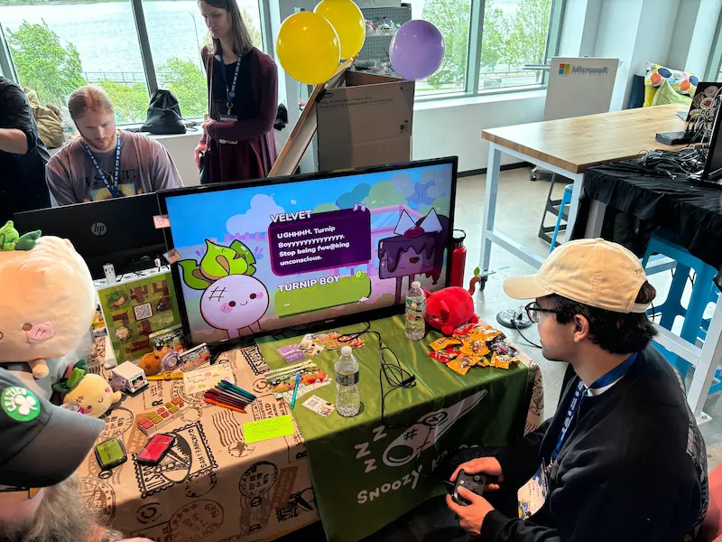 Someone playing on a controller at the Turnip Boy Steals the Mail table.